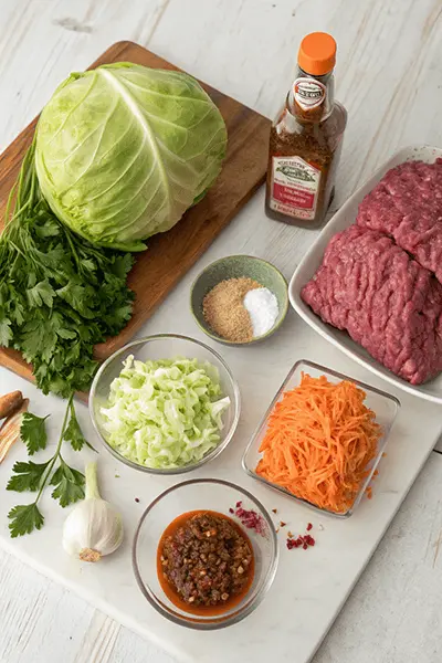 Ingredients for a ground beef cabbage recipe, including a head of cabbage, minced beef, shredded carrots, chopped cabbage, garlic, spices, and seasoning sauce.